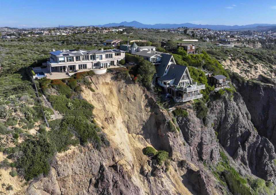 Cliff-top houses along Scenic Drive sit close to a landslide in Dana Point, Calif., on Tuesday, Feb. 13, 2024. The three homes affected by the recent deluge of rain across Orange County are being monitored but don't appear to be in imminent danger, county officials said. (Jeff Gritchen/The Orange County Register via AP)