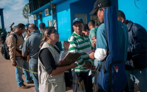 A Brazilian Health Surveillance worker talks with Venezuelans waiting in queue in front of the Brazil Federal Police Office  - Credit: MAURO PIMENTEL/AFP/Getty Images