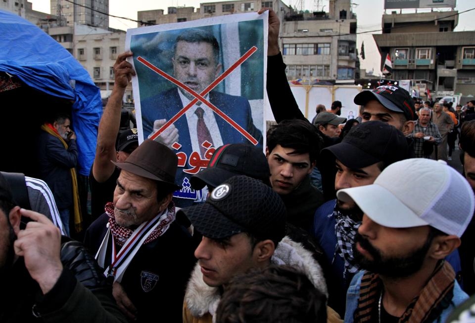 Protesters hold a poster with a defaced picture of Asaad al-Eidani, Iran-backed parliamentary bloc's nominee for the post of the prime minister and Arabic that reads "rejected by the people," in Tahrir Square during anti-government demonstrations in Baghdad, Iraq, Thursday, Dec. 26, 2019. Iraq's president refused Thursday to designate Asaad al-Eidani for the post of prime minister after he was rejected by anti-government protesters and said he was ready to submit his resignation to Parliament. (AP Photo/Khalid Mohammed)