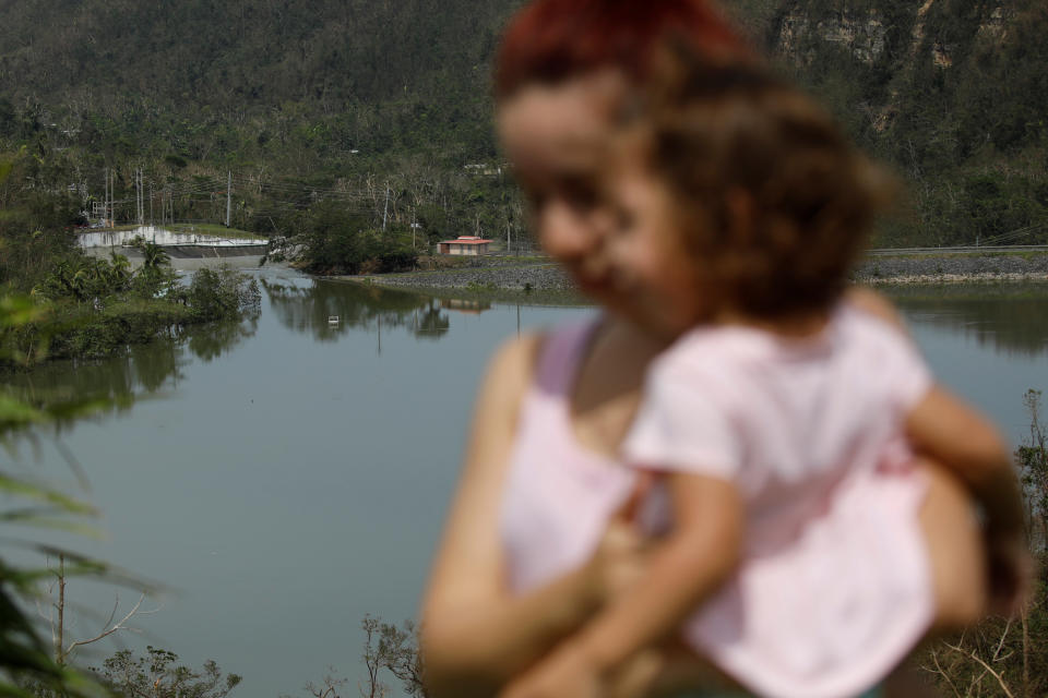 <p>Yadira Nieves carries her daughter as they look at water flowing over the road at the dam of the Guajataca lake after the area was hit by Hurricane Maria in Guajataca, Puerto Rico, Sept. 23, 2017. (Photo: Carlos Garcia Rawlins/Reuters) </p>