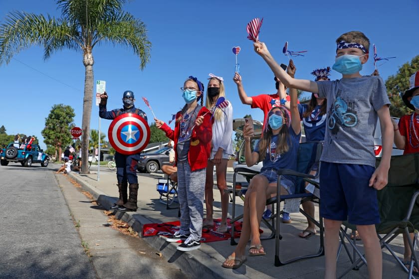 HUNTINGTON BEACH, CA - JULY 04: Mike Whitford, of Newport Beach, wearing Captain America costume, shown with his family and the Schmidgall Family, as the OneHB Neighborhood Parade passes by celebrating the Fourth of July with two vehicle caravans traveling on separate routes, passing within a mile of every single home in Huntington Beach, on Saturday, July 4, 2020 in Huntington Beach, CA. The 2020 Huntington Beach Main Street 4th of July Parade is modified and did not happen on Main Street due to Statewide COVID-19 restrictions on large events. (Gary Coronado / Los Angeles Times)
