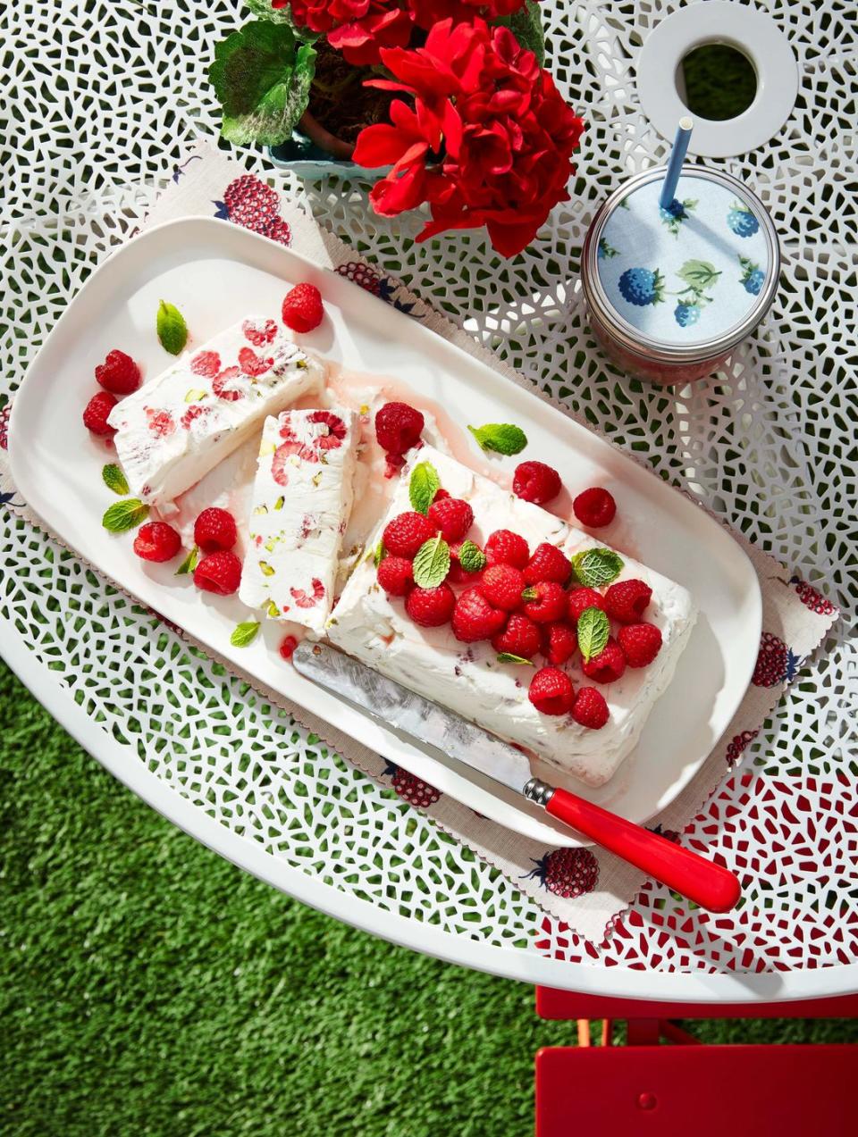 a loaf of raspberry and pistachio semifreddo on an outdoor table and topped with fresh raspberries and mint leaves for garnish