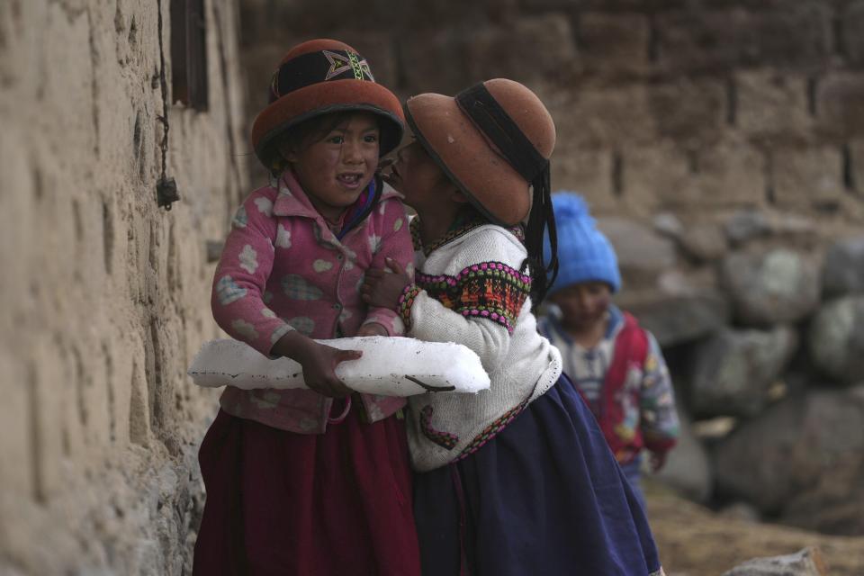 Girls play with a block of ice pieced togehter from sleet that fell the day before on the Cconchaccota community, in the Apurimac region of Peru, Saturday, Nov. 26, 2022. Peasants of the Andes in various regions of Peru and Bolivia are praying for rain amidst an ongoing drought. (AP Photo/Guadalupe Pardo)