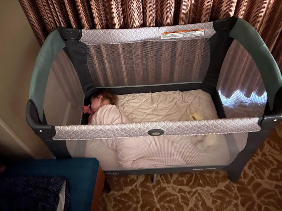 A child sleeping in a crib next to a curtained window.