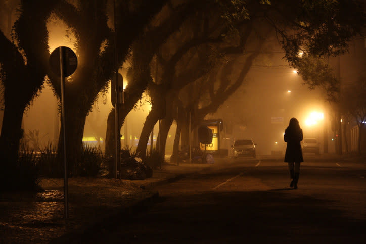 Silhouette of woman walking down tree-lined road