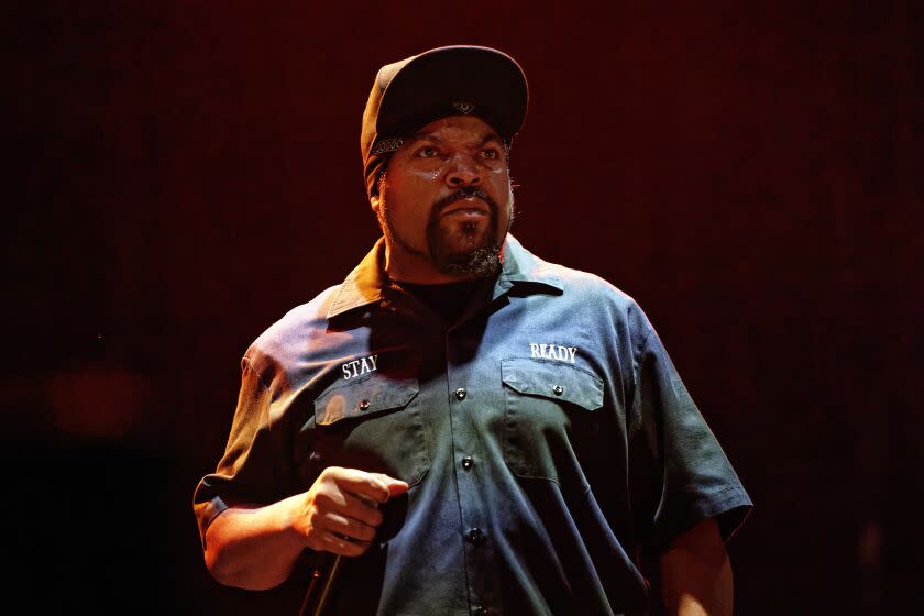 A man with a beard wearing a hat and a collared shirt and holding a microphone