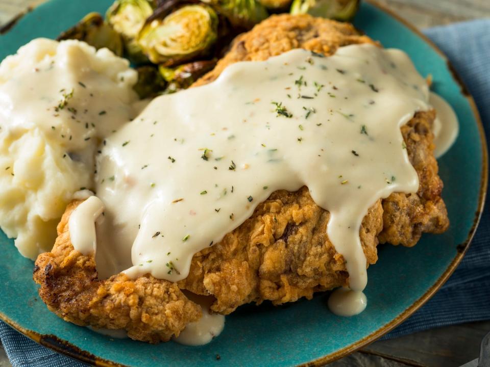 Chicken-fried steak with mashed potatoes, brussel sprouts and white gravy on top