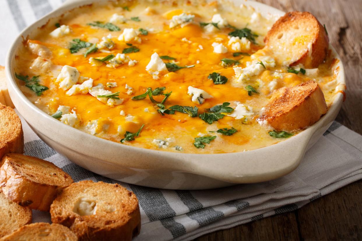 Buffalo chicken dip in a beige ceramic bowl with round bread pieces on a navy and white napkin on a rustic wooden table