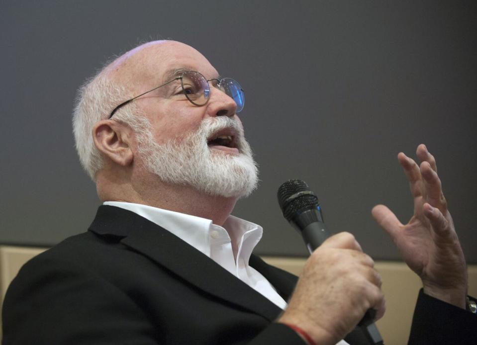 Father Gregory Boyle pictured from the shoulders up, gesturing as he speaks into a handheld microphone