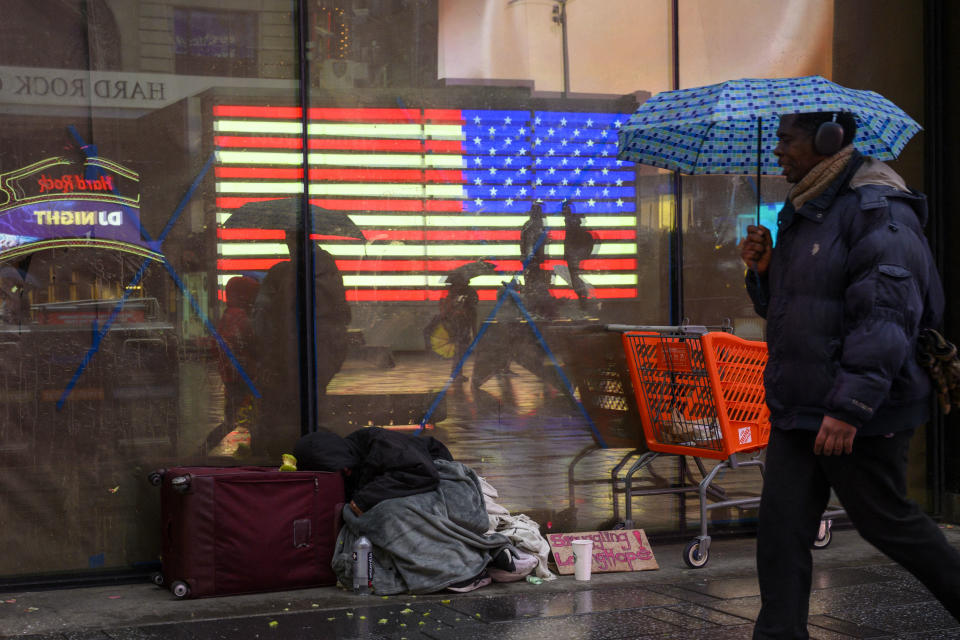 A person with an umbrella walks past a homeless person at Times Square during a rainy day on January 19, 2023 in New York City. (Photo by ANGELA WEISS/AFP)