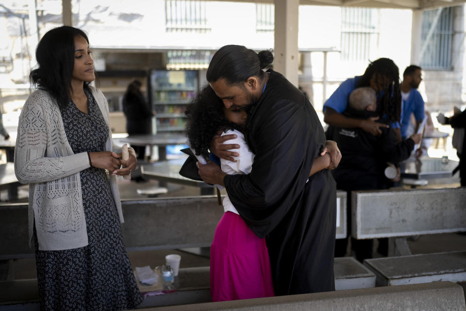 Incarcerated graduate Gerald Massey hugs his daughter, Grace, as his wife, Jacq'lene, stands next to them after his graduation ceremony at Folsom State Prison in Folsom, Calif., Thursday, May 25, 2023. Massey earned his bachelor's degree in communications through the Transforming Outcomes Project at Sacramento State. (AP Photo/Jae C. Hong)