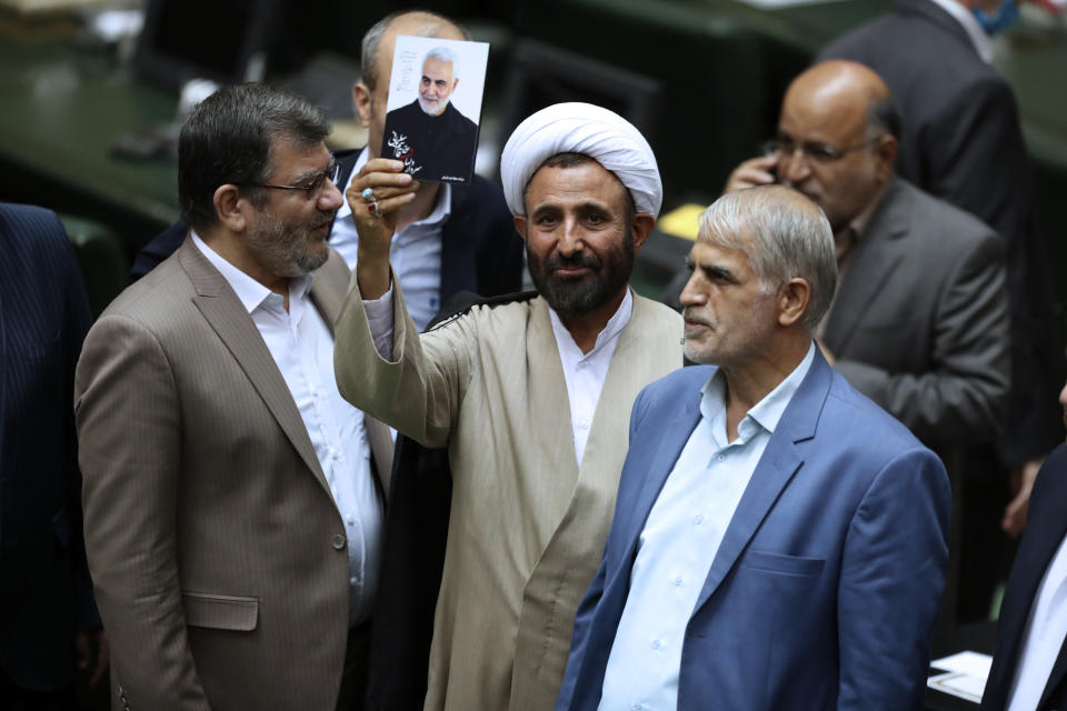 A cleric lawmaker holds a photo of Iranian Gen. Qassem Soleimani, who was killed in Iraq in a U.S. drone attack in early January 2020, during the inauguration of Iran's new parliament, in Tehran, Iran, Wednesday, May, 27, 2020. Iran has convened its newly elected parliament, dominated by conservative lawmakers and under strict social distancing regulations, as the country struggles to curb the spread of coronavirus that has hit the nation hard. Iran is grappling with one of the deadliest outbreaks in the Middle East. (AP Photo/Vahid Salemi)