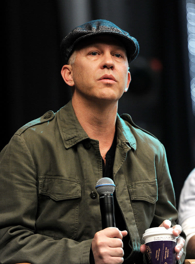 A closeup of Ryan onstage during a panel holding a mic and a to-go cup of coffee