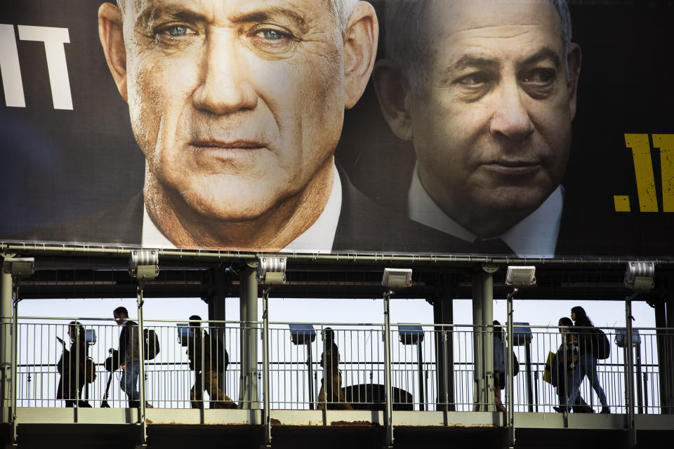 FILE - In this Feb. 18, 2020 file photo, People walk on a bridge under an election campaign billboard for the Blue and White party, the opposition party led by Benny Gantz, left, in Ramat Gan, Israel. Prime Minister Benjamin Netanyahu of the Likud party is pictured at right. Israel finds itself in a familiar place after a tumultuous election campaign, with iconoclastic politician Avigdor Lieberman seemingly in control of the country’s fate. Opinion polls ahead of the March 2 vote show that neither Netanyahu nor his challenger Gantz will be able to form a coalition government without him. Lieberman remains cagey about his intentions, raising the possibility his brinkmanship could end up forcing yet another election.(AP Photo/Oded Balilty)