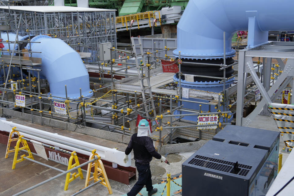 A worker walks by a blue pipe at the Fukushima Daiichi nuclear power plant, operated by Tokyo Electric Power Company Holdings, also known as TEPCO, in Futaba town, northeastern Japan, Friday, July 14, 2023. Tomohiko Mayuzumi, a TEPCO spokesperson, says treated radioactive water will be diluted with more than hundred times the seawater in the blue pipe to levels much safer than international standards, before released into the sea. (AP Photo/Hiro Komae)