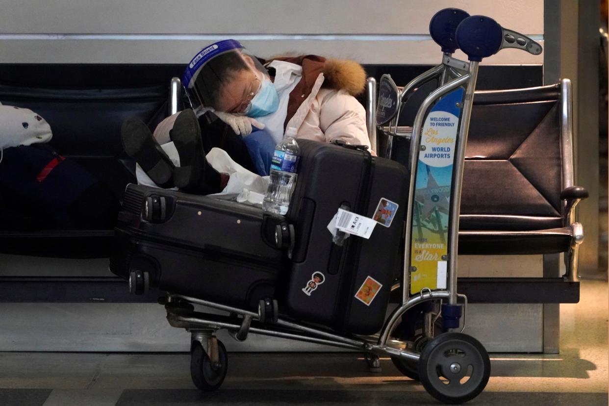 FILE - A traveler sleeps while waiting at a terminal at the Los Angeles International Airport Wednesday, Dec. 23, 2020, in Los Angeles. Among the slow trickle of information coming out of China in advance of next February's Olympics was news that, with only a handful of flights operating between the U.S. and China, American Olympians will most likely reach Beijing through a still-undetermined set of connecting flights that could more than double their travel time.(AP Photo/Marcio Jose Sanchez, File)