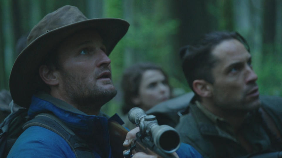 Jason Clarke anxiously looks up in the forest while holding a scoped rifle in Dawn of the Planet of the Apes.
