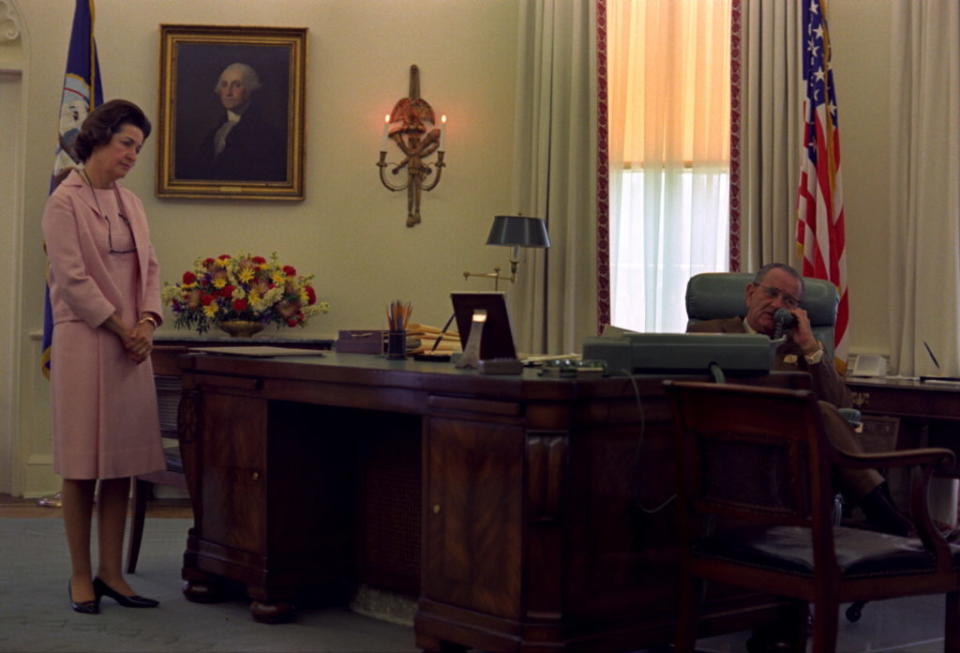 LBJ sits behind the Johnson desk with his wife Claudia "Lady Bird" Johnson by his side.