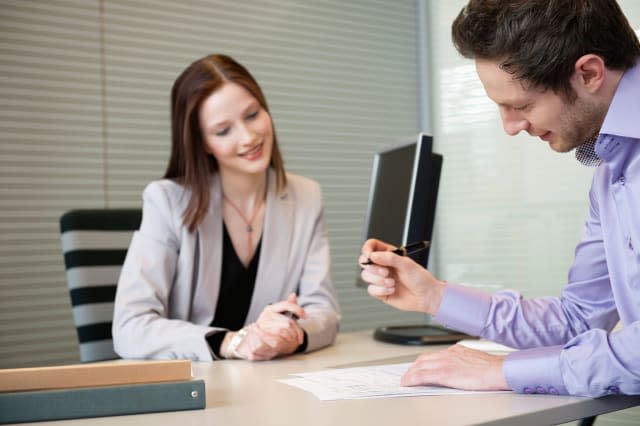 BP6MH2 Man signing documents with a female real estate agent sitting in front of him  man; signing; documents; agreement; woman;