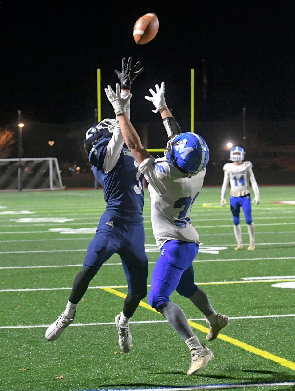 Kayden Eaton, of Mashpee, and Thomas Hansen, of Cohasset, reach for a Mashpee pass at the end of the first half in the Division 7 state semifinal football game in Carver on Nov. 19, 2021.  The pass fell incomplete.