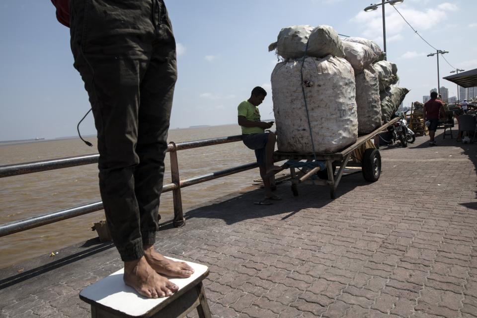 In this Sept. 1, 2019 photo, a vendor looks at his cell phone while a man on a stool practices capoeira at the Ver-o-Peso riverside market in Belém, Brazil. Capoeira is an Afro-Brazilian martial art that combines elements of dance, acrobatics and music. It was developed by enslaved Africans in Brazil. (AP Photo/Rodrigo Abd)