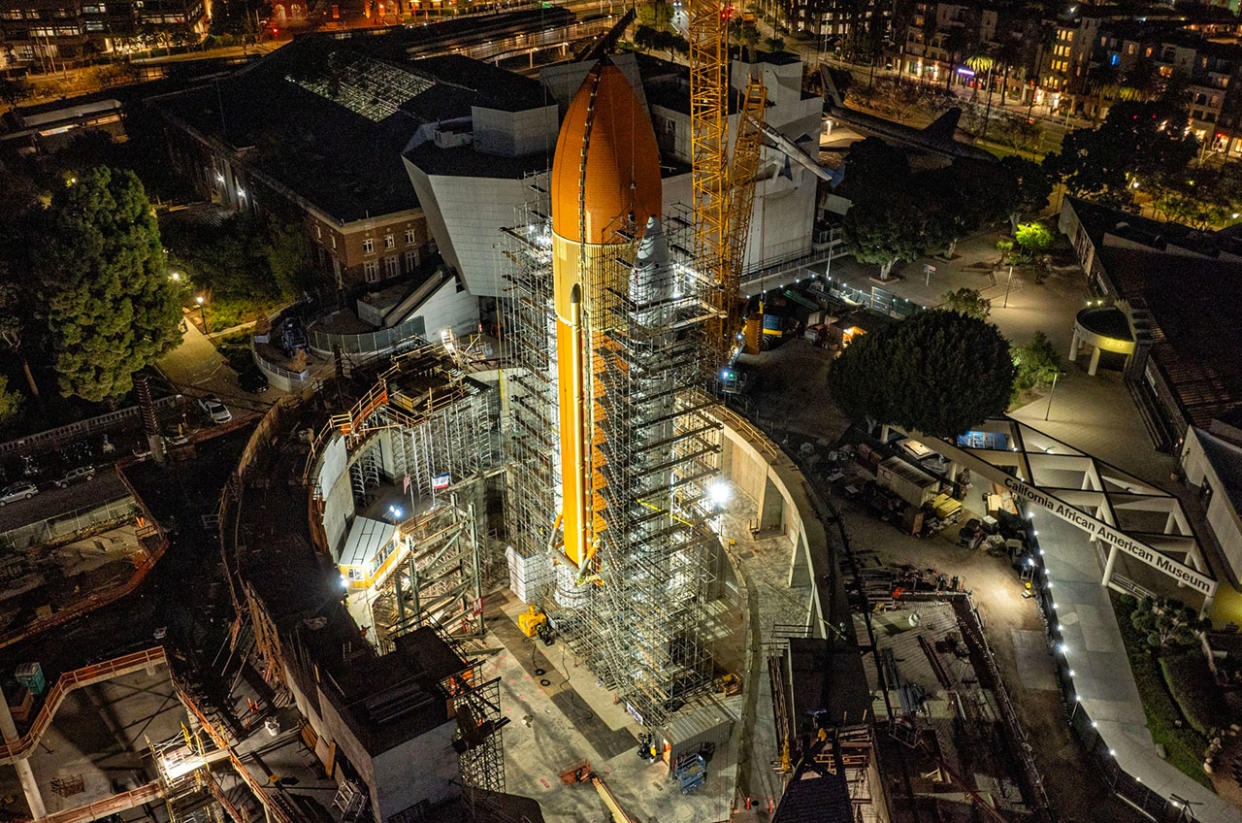  A large orange cylindrical tank stands at night, surrounded by metallic scaffolding. 