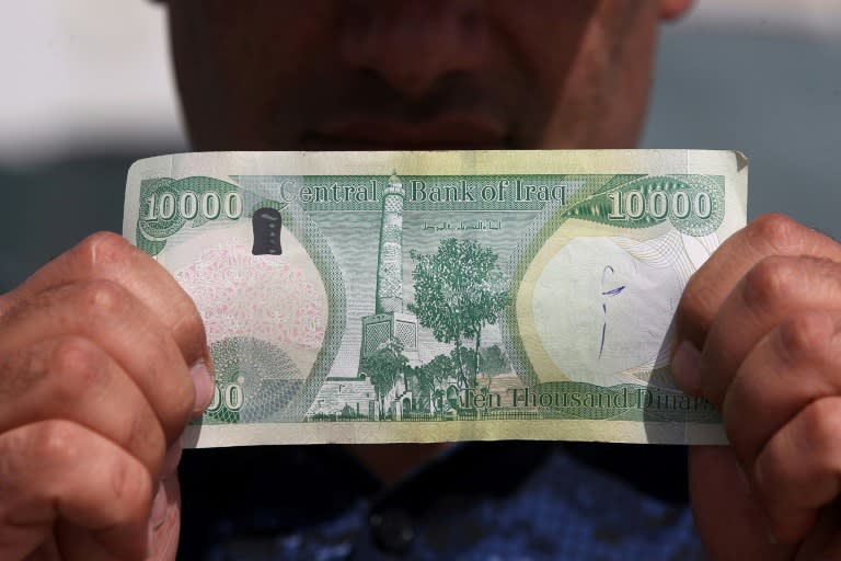 An Iraqi policeman shows a 10,000-dinar banknote bearing an image of Mosul's iconic leaning minaret, known as the "Hadba" (Hunchback), on June 22, 2017, in Mosul