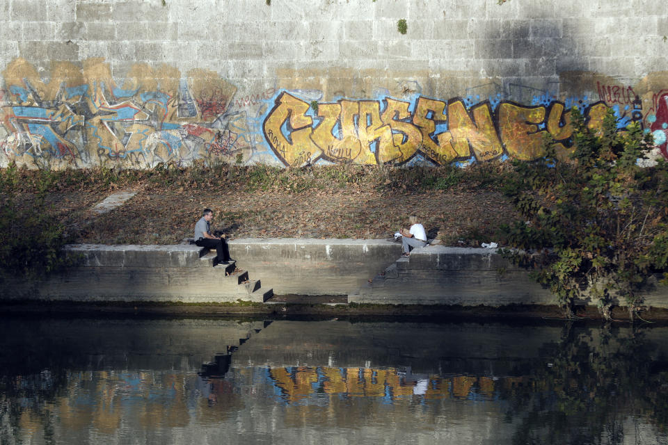 People sit on the Tiber river banks covered in fallen leaves and overgrown grass, backdropped by graffiti filled walls, in Rome, Thursday, Nov. 15, 2018. Rome’s monumental problems of garbage and decay exist side-by-side with Eternal City’s glories. (AP Photo/Gregorio Borgia)