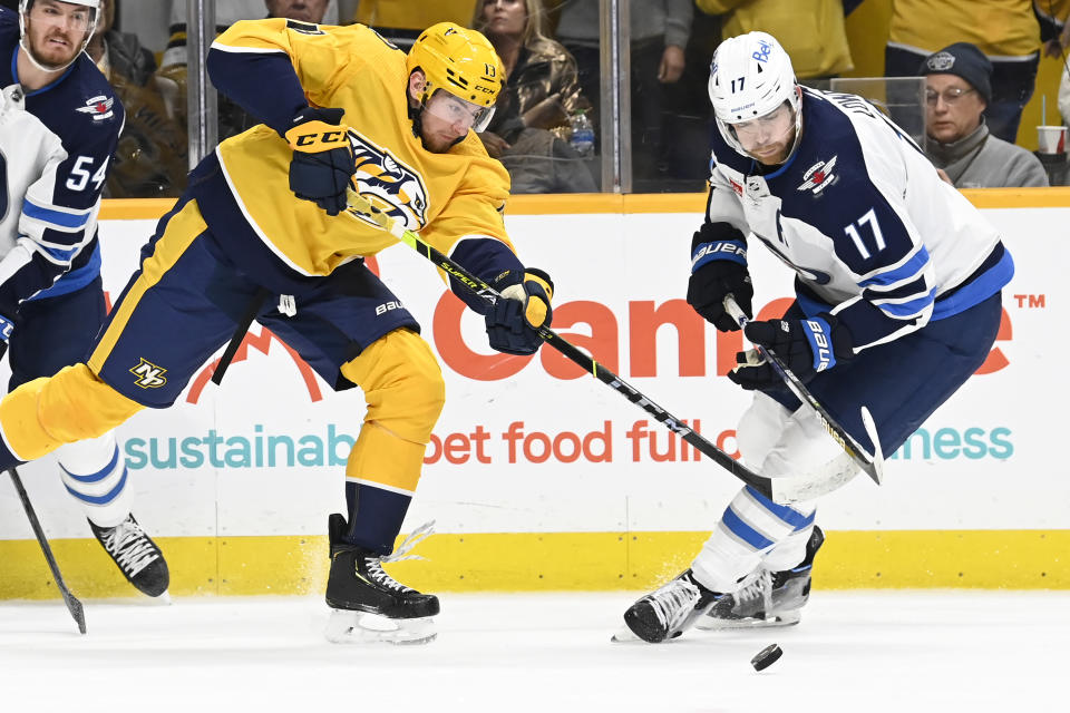 Nashville Predators center Yakov Trenin (13) and Winnipeg Jets center Adam Lowry (17) go for the puck during the second period of an NHL hockey game Saturday, March 18, 2023, in Nashville, Tenn. (AP Photo/Mark Zaleski)