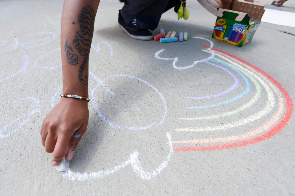 Former Kickapoo student Zari Black, 21, draws a rainbow in chalk on the sidewalk outside of Kickapoo High School during a protest outside the school on Monday.