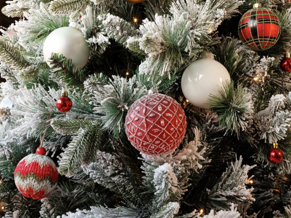 white and red ornaments hanging from a snow-dusted christmas tree