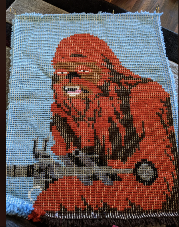 A crochet wall hanging featuring Chewbacca from Star Wars, carefully detailed with a blaster in hand