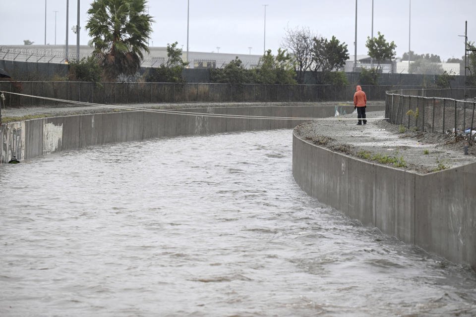 A person monitors water flowing in the Ormond Lagoon Waterway, Thursday, Dec. 21, 2023, in Port Hueneme, Calif. Downpours Thursday targeted coastal Ventura and Santa Barbara counties northwest of Los Angeles County, swamping areas in the cities of Oxnard, Port Hueneme and Santa Barbara. Port Hueneme officials issued evacuation orders for residences on four streets, and an evacuation center was set up at a college gymnasium. (AP Photo/Michael Owen Baker)