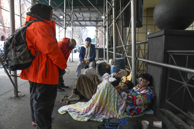 FILE - Recent immigrants to the United States lie on the sidewalk with their belongings as they talk to city officials in front of the Watson Hotel in New York, Monday, Jan. 30, 2023. Around Manhattan and elsewhere in the city, hotels that served tourists just a few years ago have become de facto emergency shelters. The latest is the historic Roosevelt Hotel in midtown Manhattan, which shuttered three years ago, is reopening later this week as a welcome center and shelter for asylum seekers. (AP Photo/Seth Wenig, File)