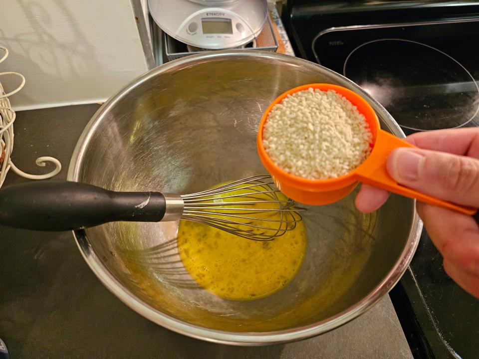 Measuring cup of bread crumbs above a bowl of whisked egg