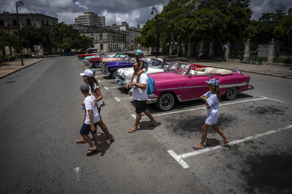 Tourists walk past a parking lot full of classic American cars waiting for customers, in Havana, Cuba, Saturday, July 9, 2022. Hotels and air routes closed for more than a year due to the restrictions related to the coronavirus pandemic have been reopening, something crucial for a country that depends heavily on foreign tourism for the hard currency needed to import food and other crucial goods. (AP Photo/Ramon Espinosa)