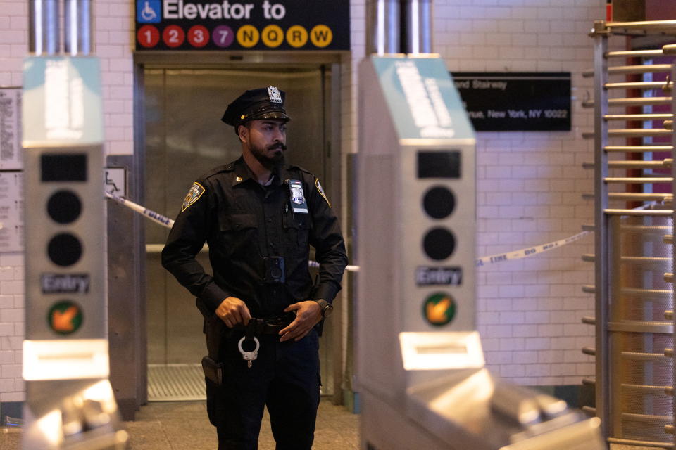 An NYPD officer seen through a fare scanner in front of a subway elevator.