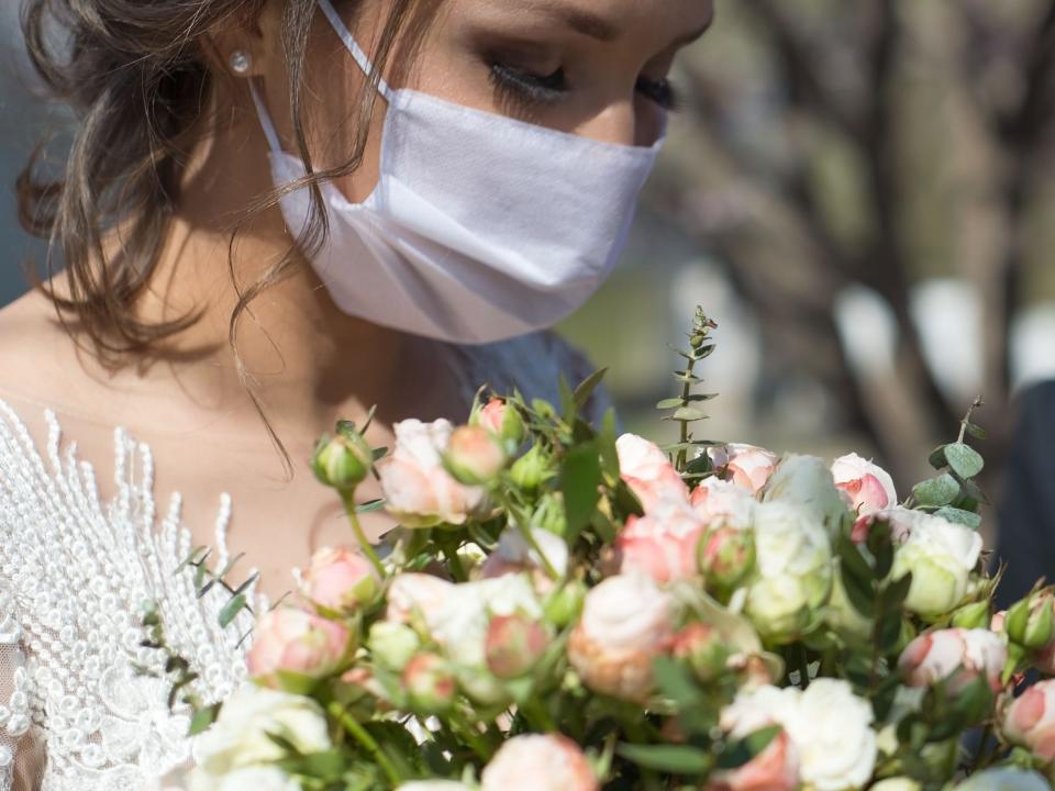 A bride wears a mask and holds a bouquet of flowers