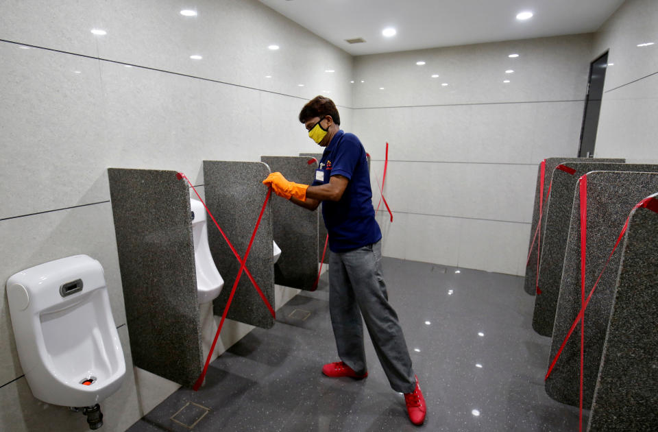 A worker applies tape markings on urinals to encourage social distancing at a shopping mall after authorities allowed malls to reopen as India eases lockdown restrictions that were imposed to slow the spread of the coronavirus disease (COVID-19), in Ahmedabad, India, June 8, 2020. REUTERS/Amit Dave