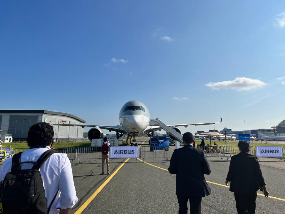 A front-view of the Qatar Airbus A350, with people in the foreground walking towards it and an Airbus banner.
