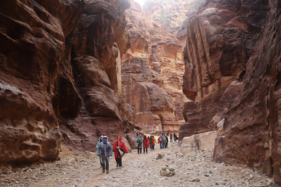 FILE - In this Feb. 13, 2017 file photo, tourists brave a rare rainstorm in plastic ponchos to hike deeper into Jordan's famous Petra archaeological park, southern Jordan. In ancient times, Arab tribesmen dug diversion tunnels to protect their low-lying trading post of Petra against desert flash floods. More than two millennia later, an alarm system warns visitors if flood water rushes toward what has become Jordan's main tourist attraction. (AP Photo/Sam McNeil, File)