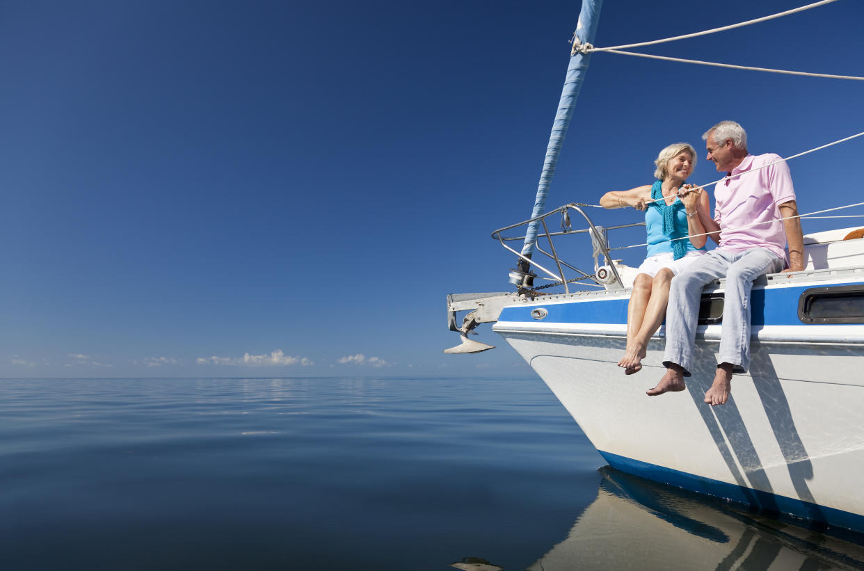 A happy senior couple sitting on the front of a sail boat on a calm blue sea