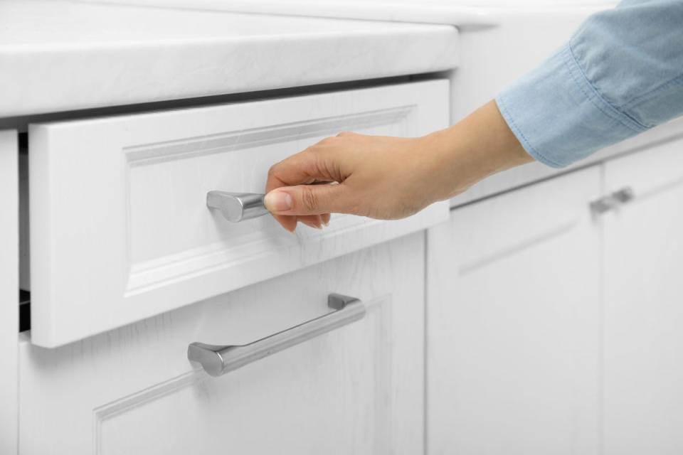 Person opening drawer in all-white kitchen cabinetry.