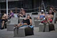FILE - In this Tuesday, June 8, 2021 file photo, people sunbathe near the beach in Barcelona, Spain. For Europe’s battered tourism industry, chaos and confusion over travel rules and measures to contain fresh virus outbreaks are contributing to another cruel summer. Popular destination countries are grappling with surging COVID-19 variants but the patchwork and last-minute nature of the efforts as peak season gets underway threatens to derail another summer. (AP Photo/Emilio Morenatti, File)