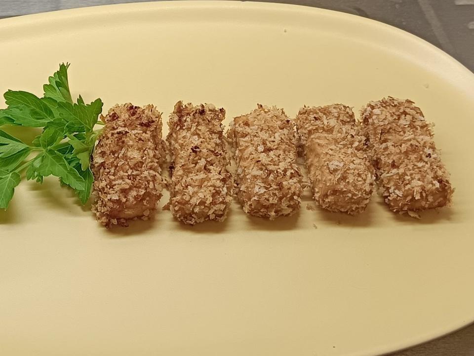 Air-fried tofu on a yellow plate with a sauce and sprig of parsley next to it