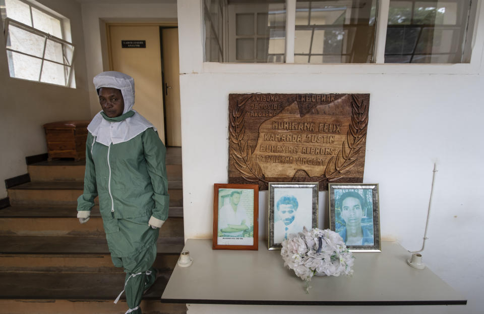 In this photo taken Thursday, Nov. 7, 2019, a worker who makes liquid morphine from powder wears protective clothing to protect from the effects of the drug and to prevent contamination, as she walks past a memorial to the four people working at the Pharmaceutical Laboratory of Rwanda who died in the country's 1994 genocide, at the facility in Butare, Rwanda. While people in rich countries are dying from overuse of prescription painkillers, people in Rwanda and other poor countries are suffering from a lack of them, but Rwanda has come up with a solution to its pain crisis - it's morphine, which costs just pennies to produce and is delivered to households across the country by public health workers. (AP Photo/Ben Curtis)