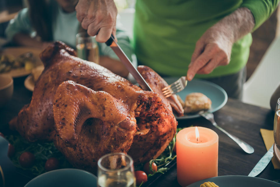 Cropped photo of family feast roasted turkey on table grandfather hands cutting meat into slices hungry relatives waiting in living room indoors