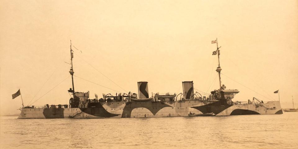 A historical black-and-white photo of the USS Minneapolis with curved, black-and-white dazzle paint, in Hampton Roads, Virginia, USA, 1917