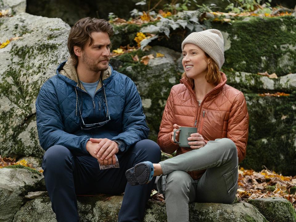 Luke Grimes as Jake and Ellie Kemper as Helen sitting on rocks in a scene from happiness for beginners