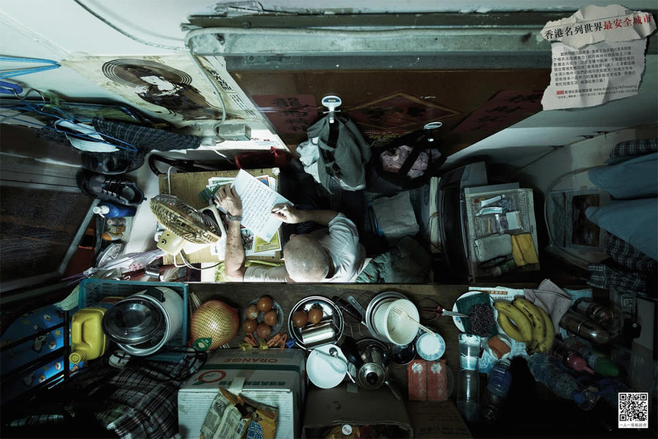 A man reads at his desk with a tiny kitchen shelf above his head.